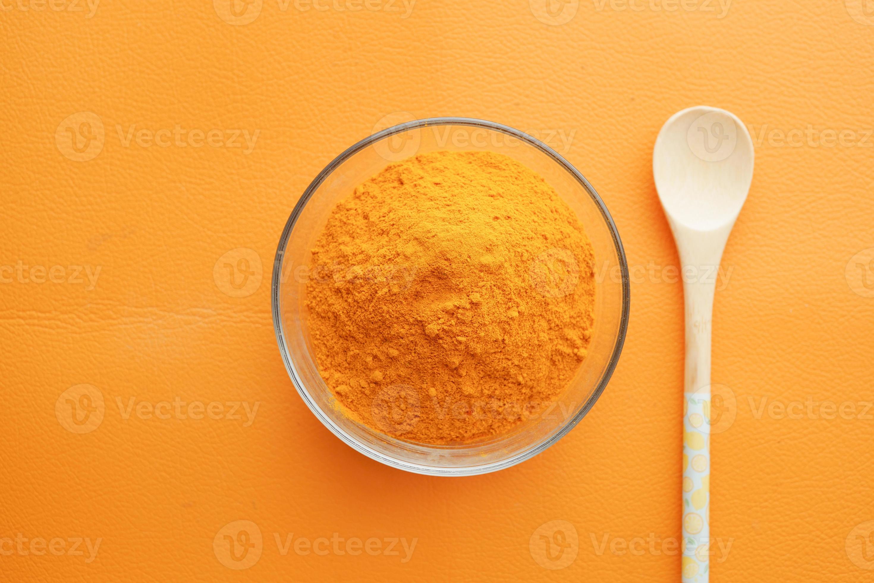 top view of turmeric root powder in bowl on orange color background