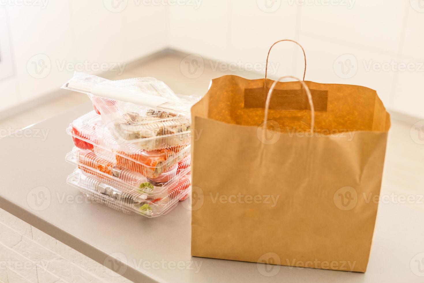 Sushi rolls in plastic box near paper package on white table. Delivery. Take away. photo