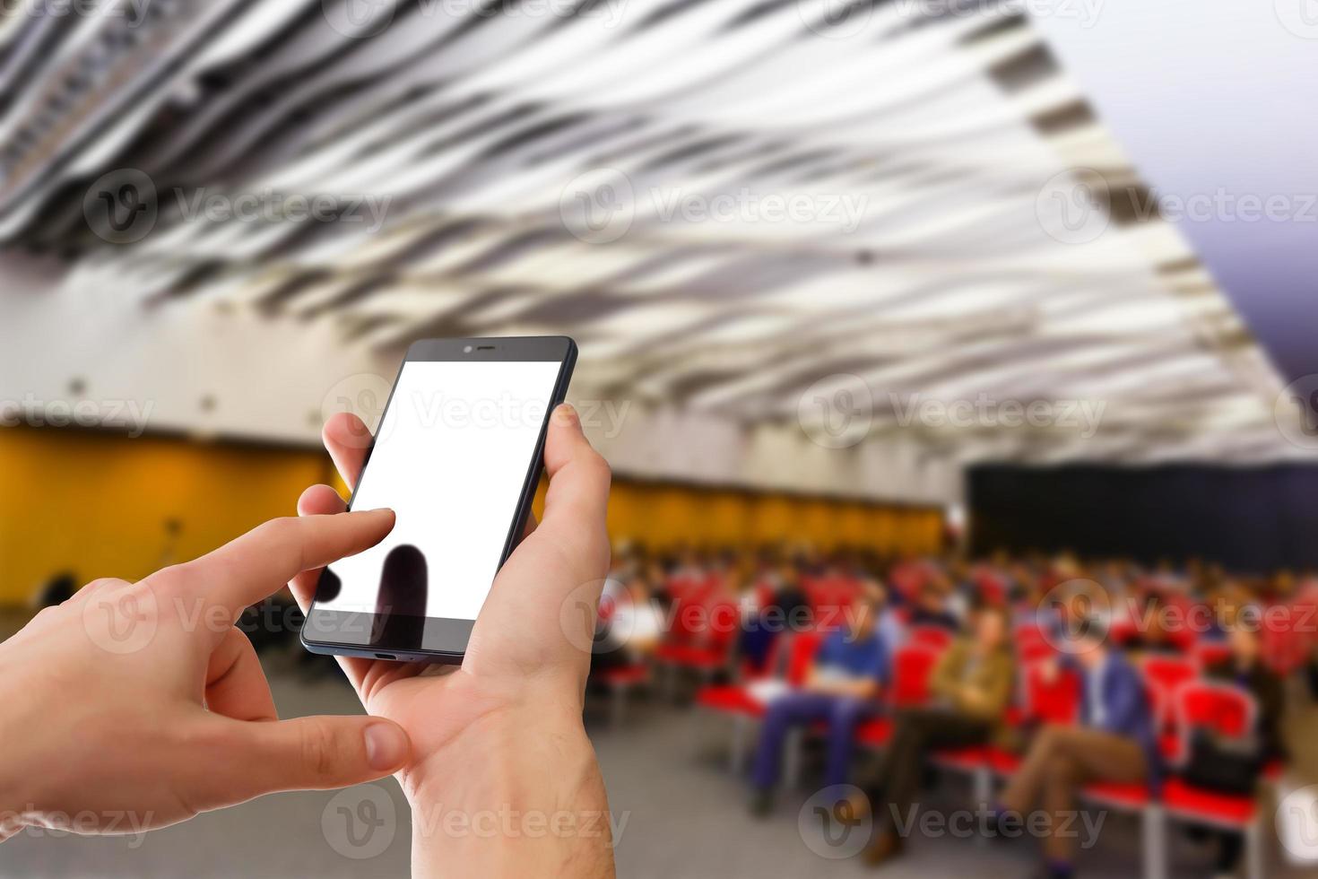 Man use mobile phone, blur image of people live in large conference room as background. photo