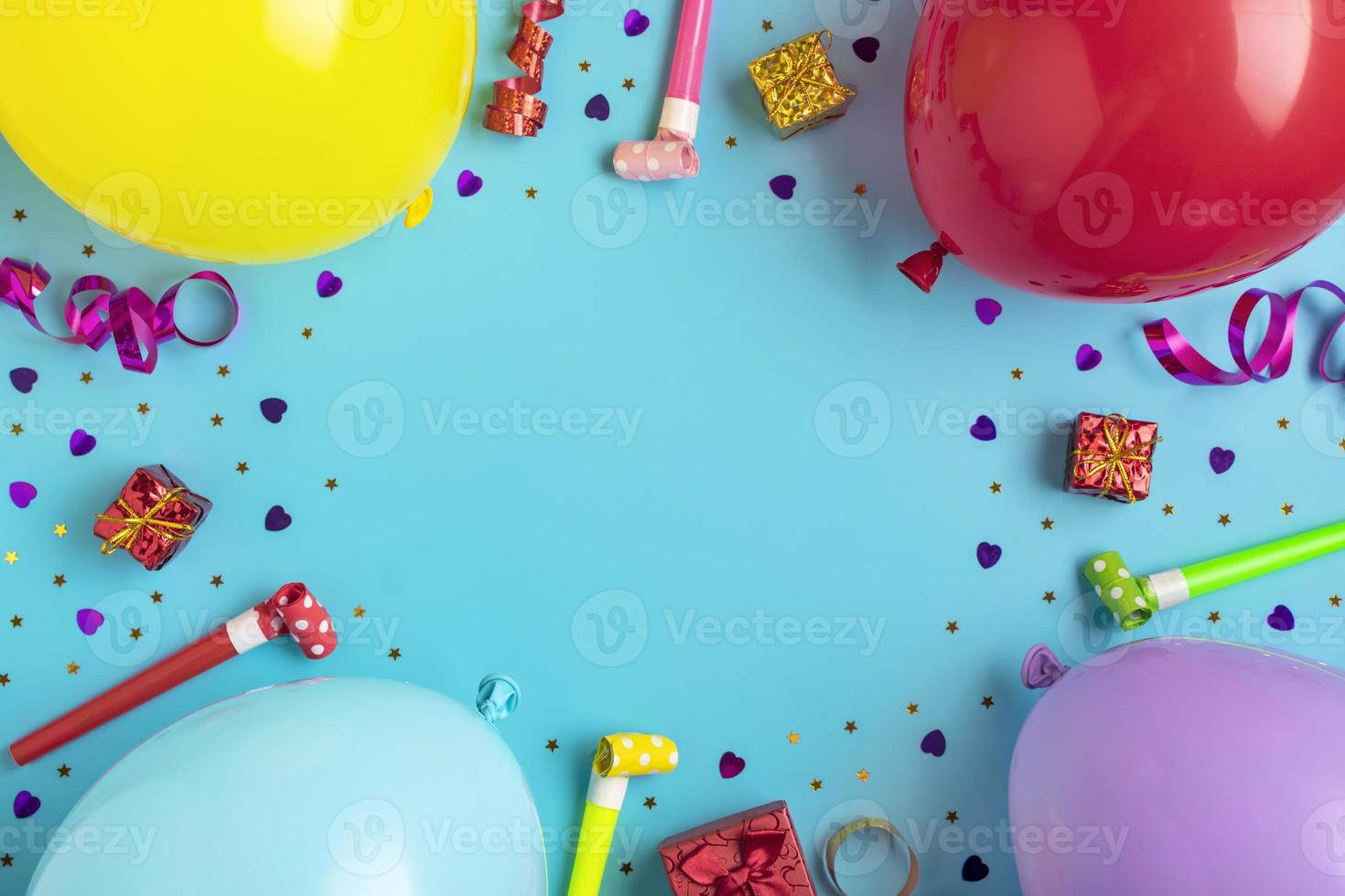 Colorful party frame with red gift box with various party confetti, balloons, streamers, pokers and decorations on blue background. Holiday card Flat lay Top view Happy Birthday party concept photo