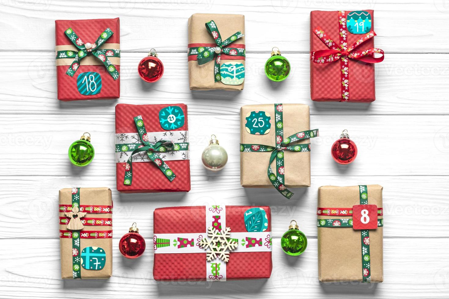 cajas de regalo rojas y verdes envueltas a mano decoradas con cintas, copos de nieve y números, adornos navideños y decoración en mesa blanca concepto de calendario de adviento de navidad vista superior tarjeta de vacaciones plana foto