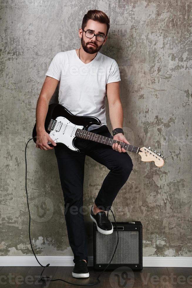 Stylish bearded guy with guitar against concrete wall photo