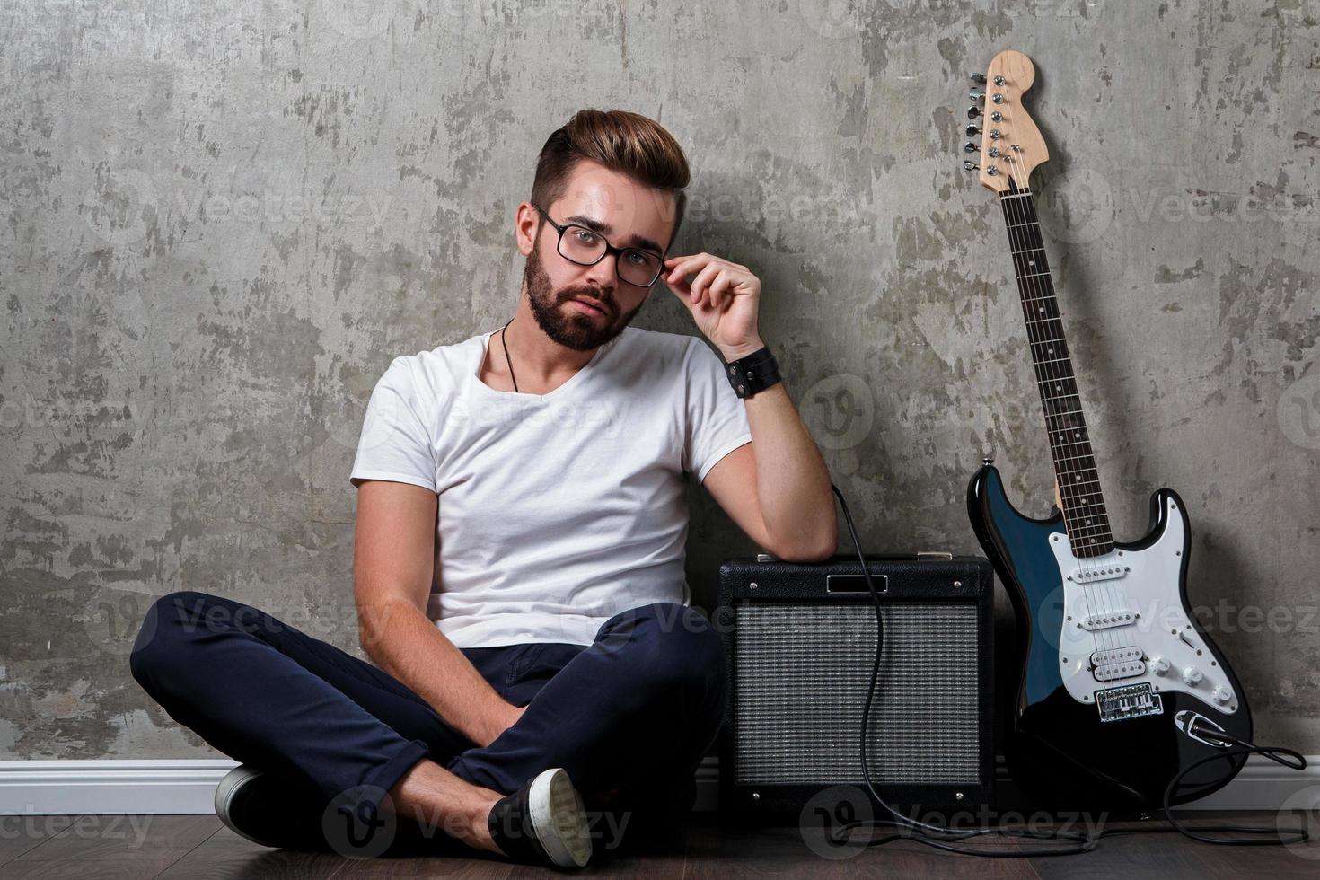 chico barbudo elegante con guitarra contra pared de hormigón foto