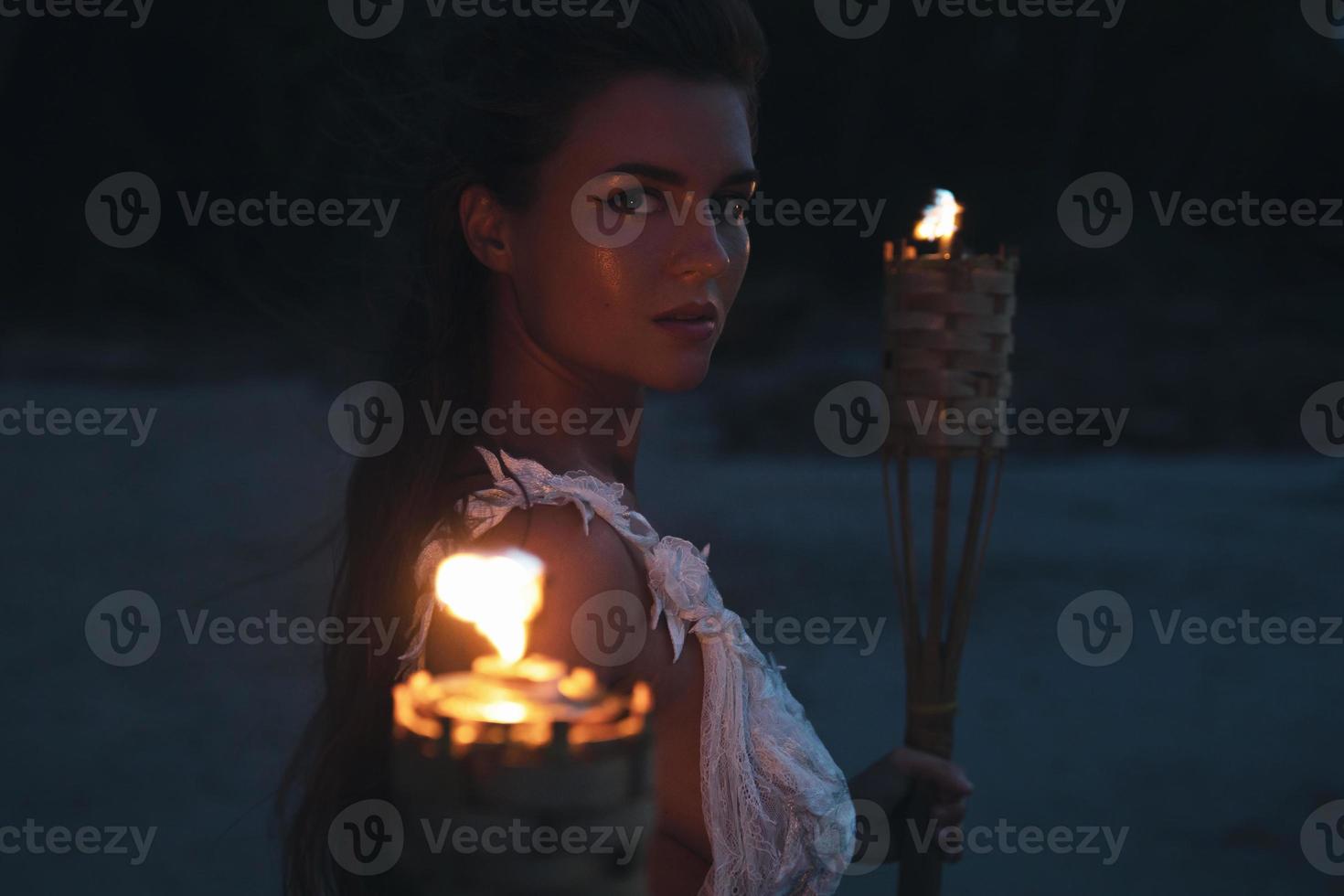 Bride in beautiful wedding dress is holding torchlight on the beach photo