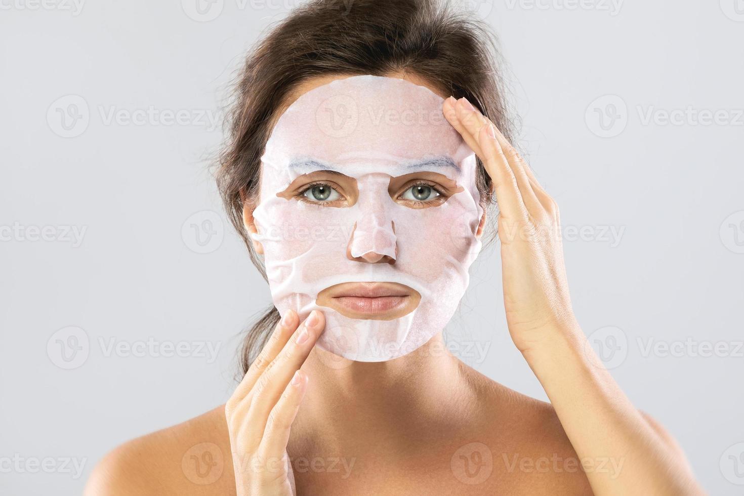 Woman with a sheet moisturizing mask on her face isolated on gray background photo