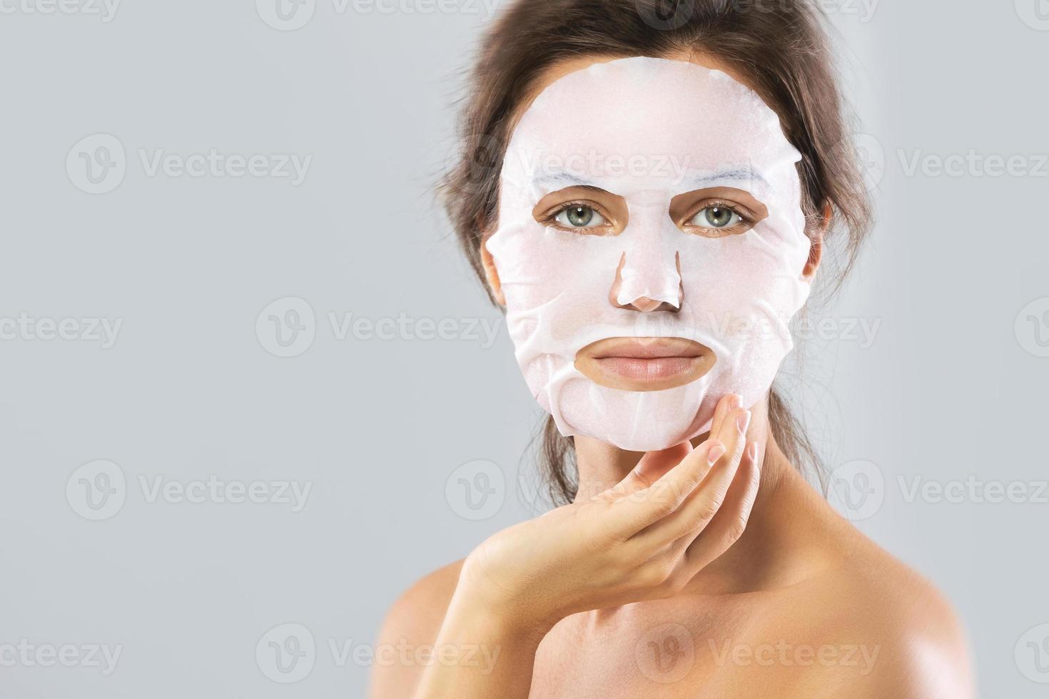 Woman with a sheet moisturizing mask on her face isolated on gray background photo