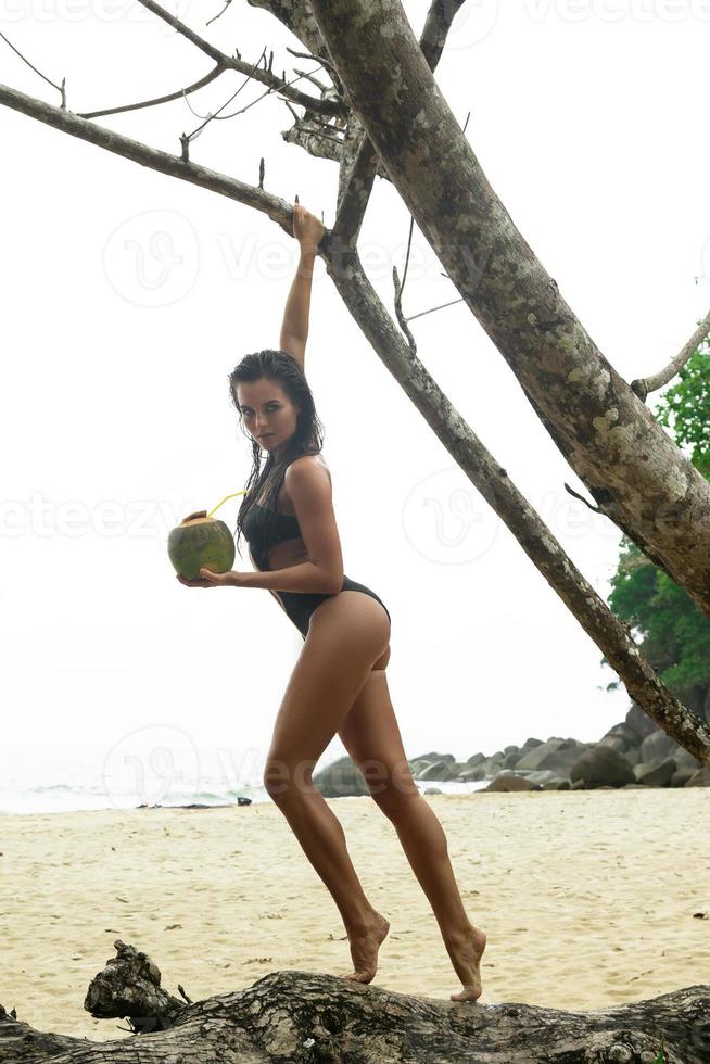 mujer sexy con cóctel de coco posando junto a un árbol viejo foto