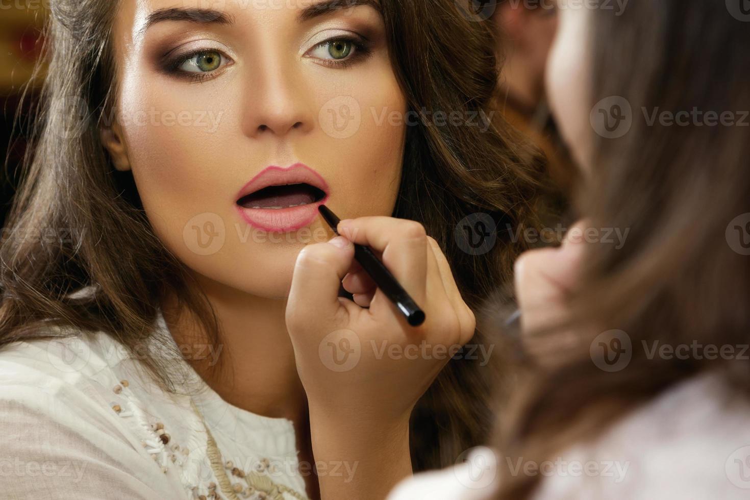Beautiful woman is using pencil for lips photo