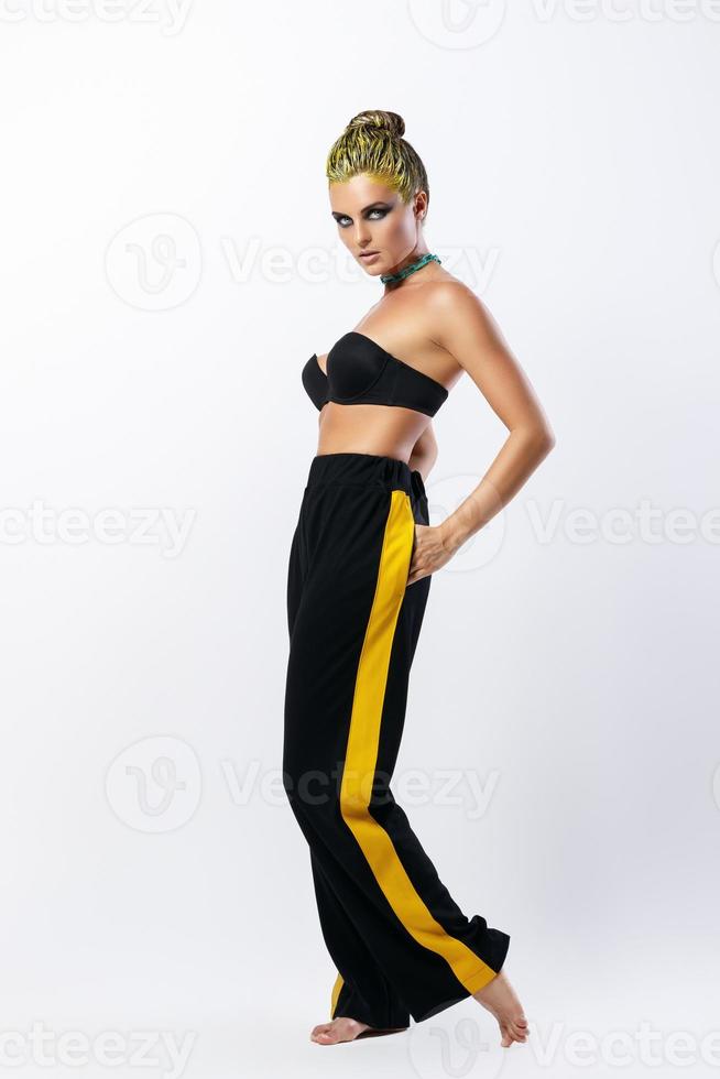 Stylish woman with yellow hair and trackpants on gray background photo