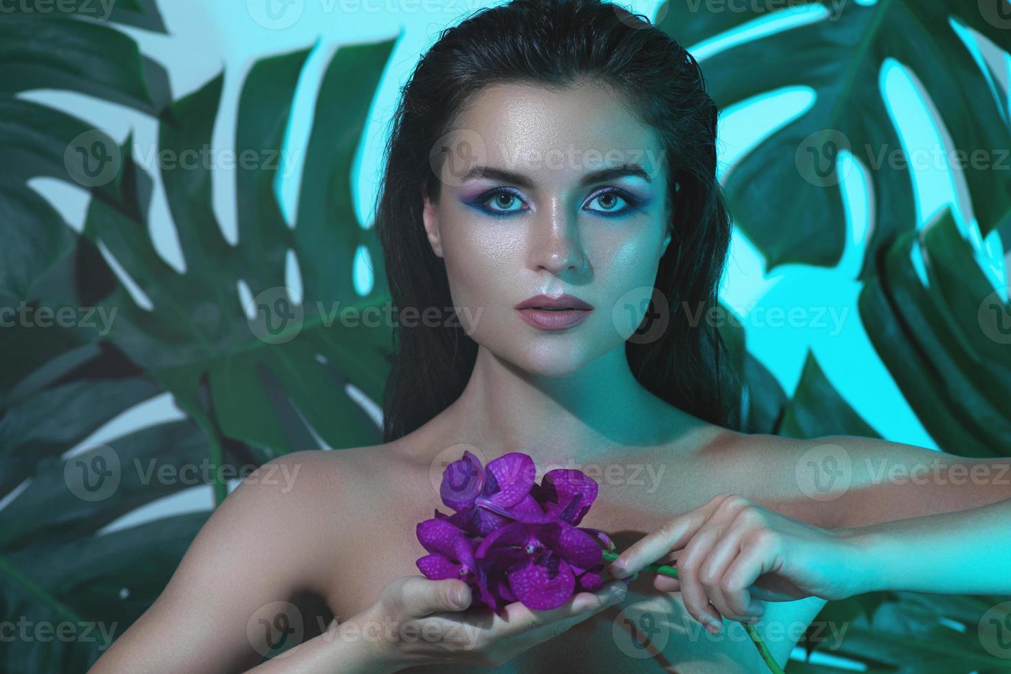 una mujer joven y hermosa con una piel suave y perfecta sostiene flores de orquídeas foto