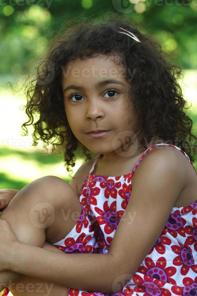 Little African girl sitting on a grass in a city park photo