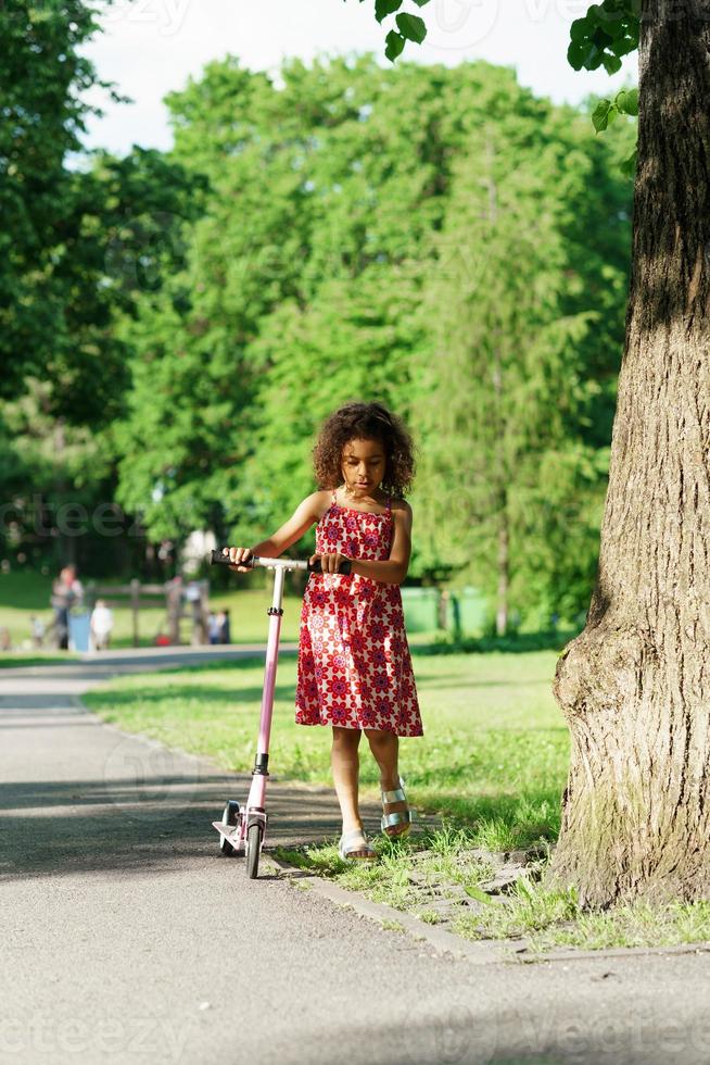 Little black girl with a kick scooter in a city park photo