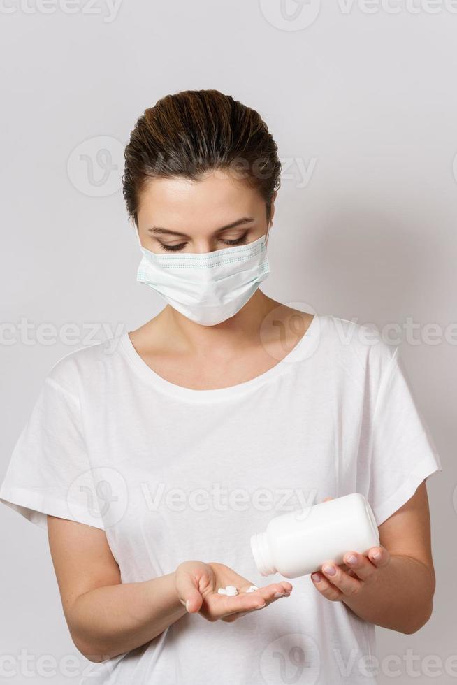 Woman wearing face mask is holding a white pills photo