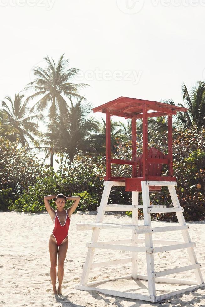 Sexy woman in red swimsuit beside lifeguard tower on the beach photo