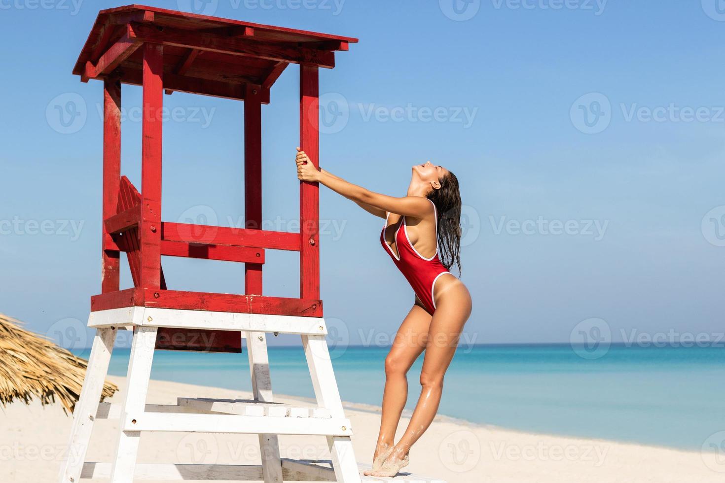 Sexy woman in red swimsuit posing beside a lifeguard tower photo