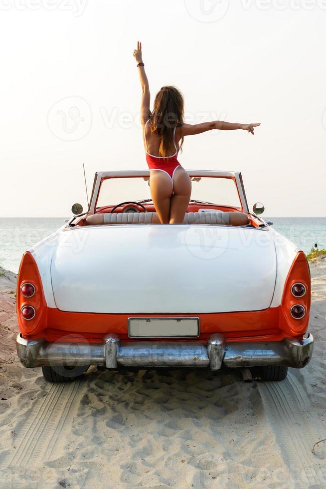 Sexy woman wearing red swimsuit is sitting inside a retro cabriolet car photo