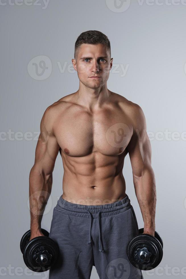 Young and muscular man working out with dumbbells photo