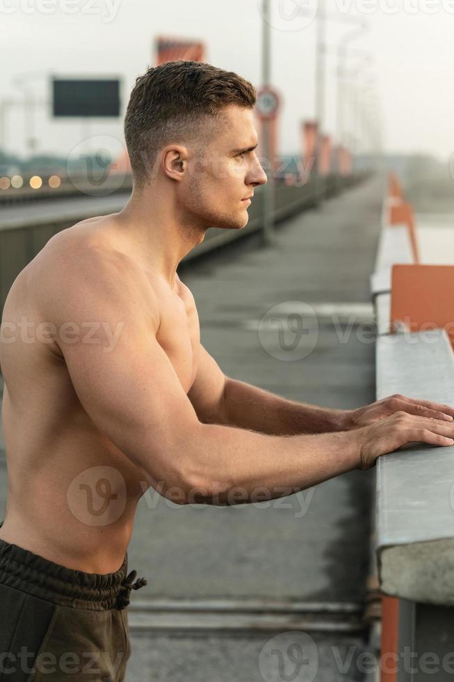 Muscular man with naked torso during fitness workout on a bridge photo