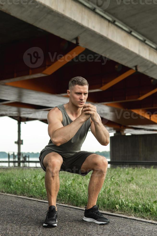 Muscular man is making squats under the bridge during his street workout photo