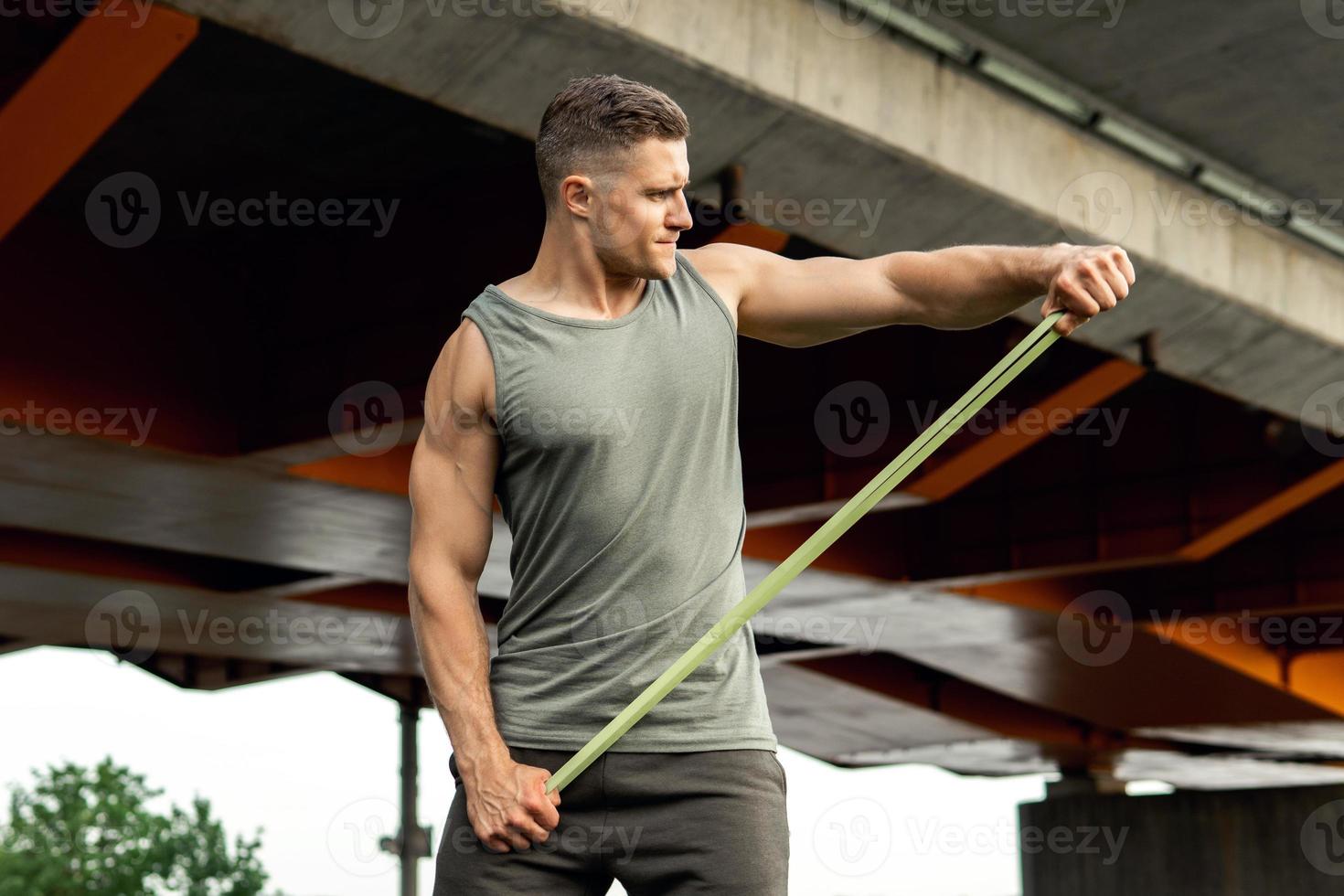 Muscular man during workout with a resistance rubber band on a street. photo