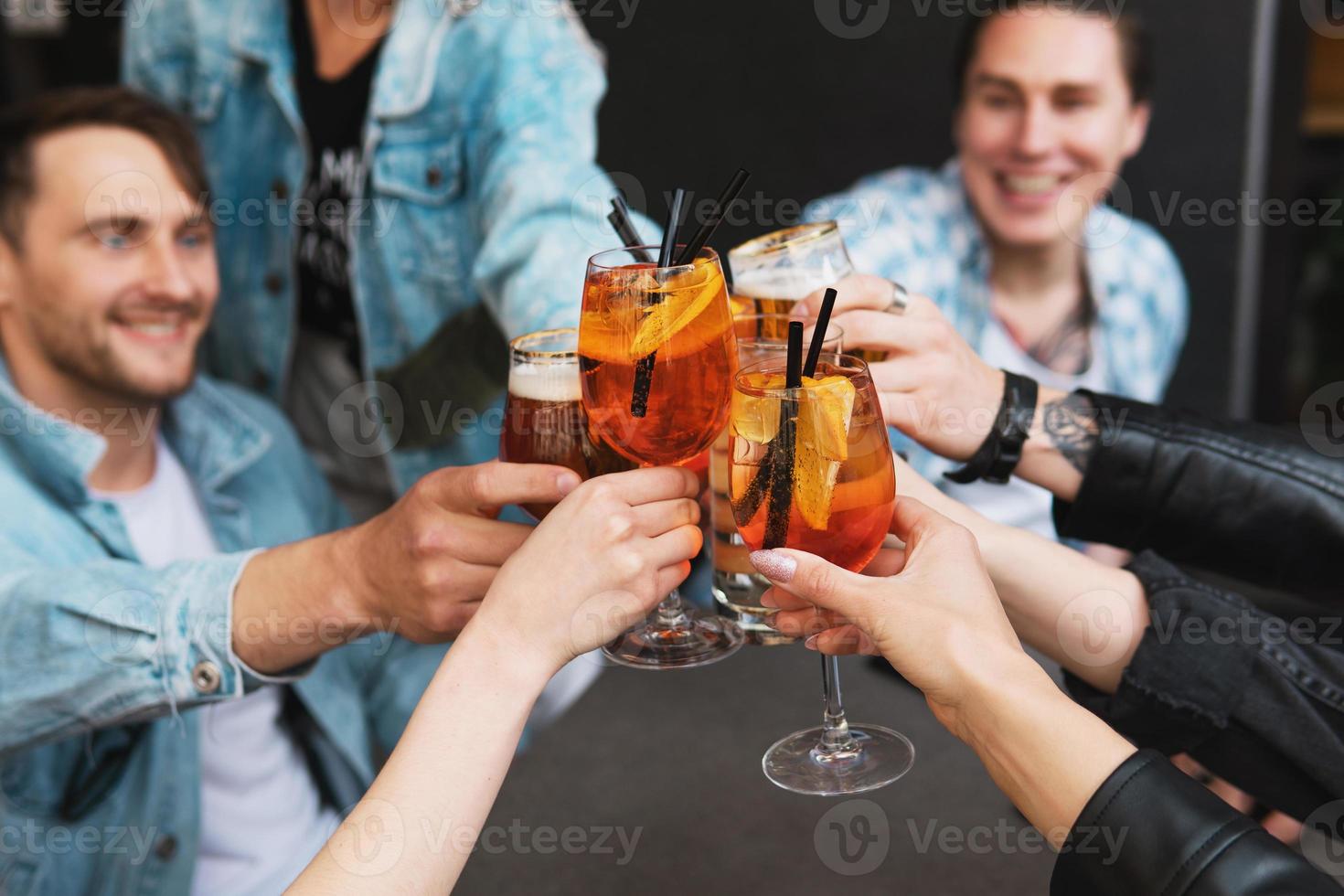 Friends celebrating and holding glasses with different alcohol drinks in a bar. photo