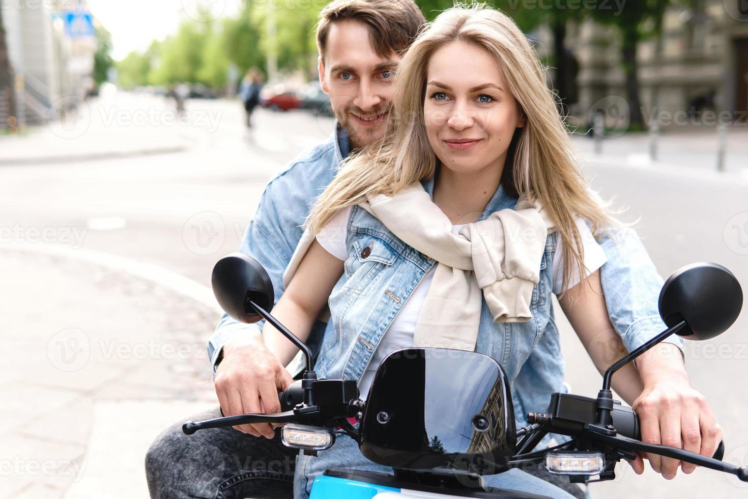 Stylish couple having fun while riding electric scooter on city street photo