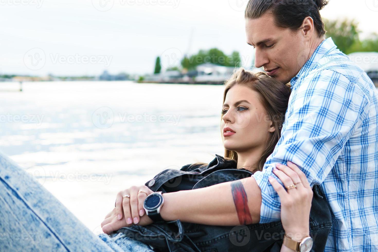 Young sensual and loving couple sitting on a pier beside a river photo