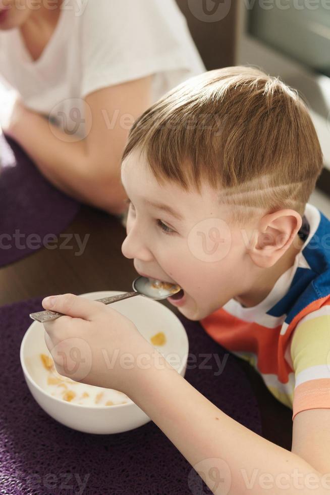 Beautiful mother and her cute son eating healthy cornflakes for breakfast photo