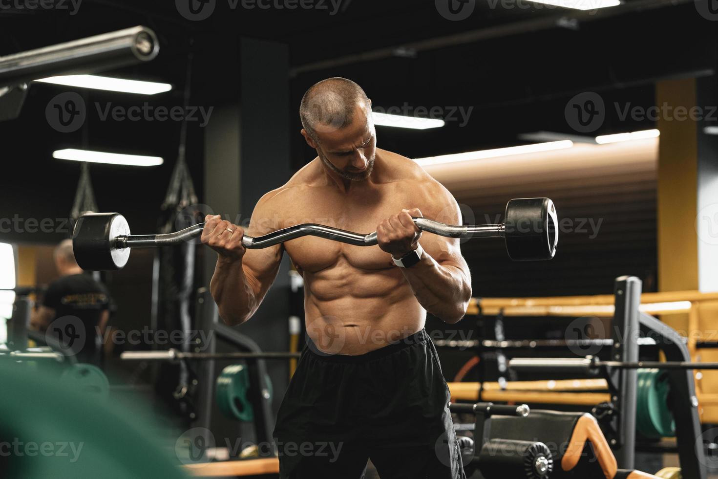Muscular bodybuilder doing biceps curls with a barbell in the gym photo