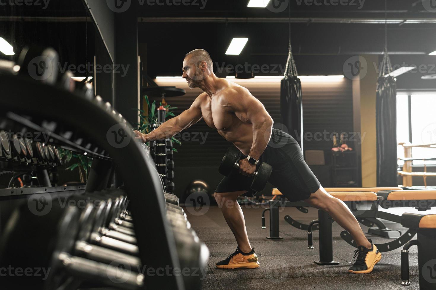 Bodybuilder doing one-arm dumbbell row during his workout in a gym photo