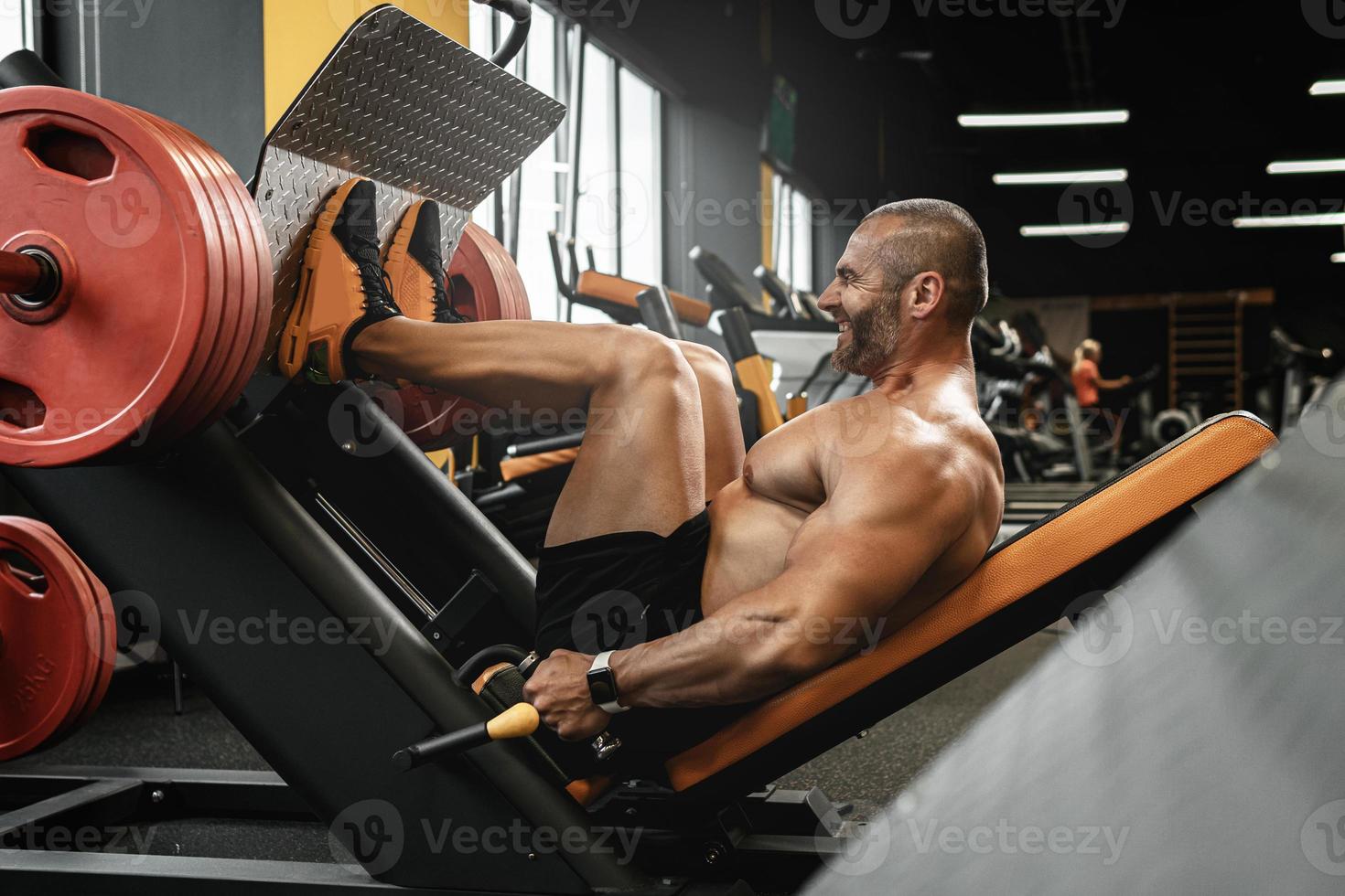 Bodybuilder doing a seated leg press exercise in a gym photo