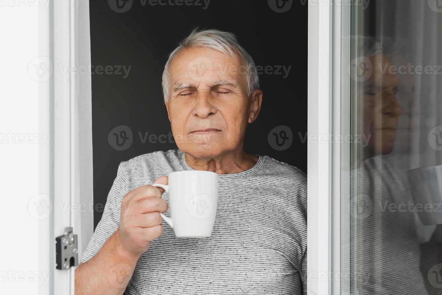 Elderly man with a cup of coffee looking into the window photo