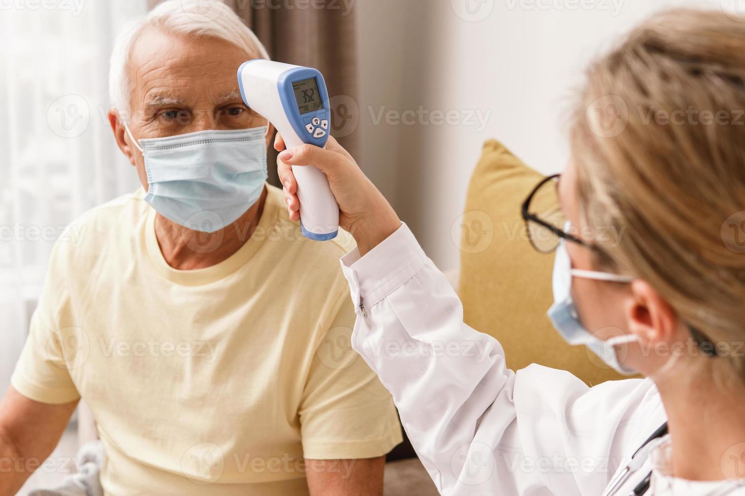 Doctor checking body temperature to elderly man during home visit photo