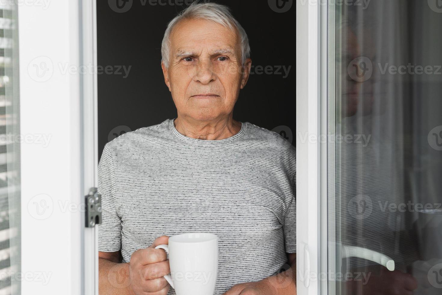 Elderly man with a cup of coffee looking into the window photo
