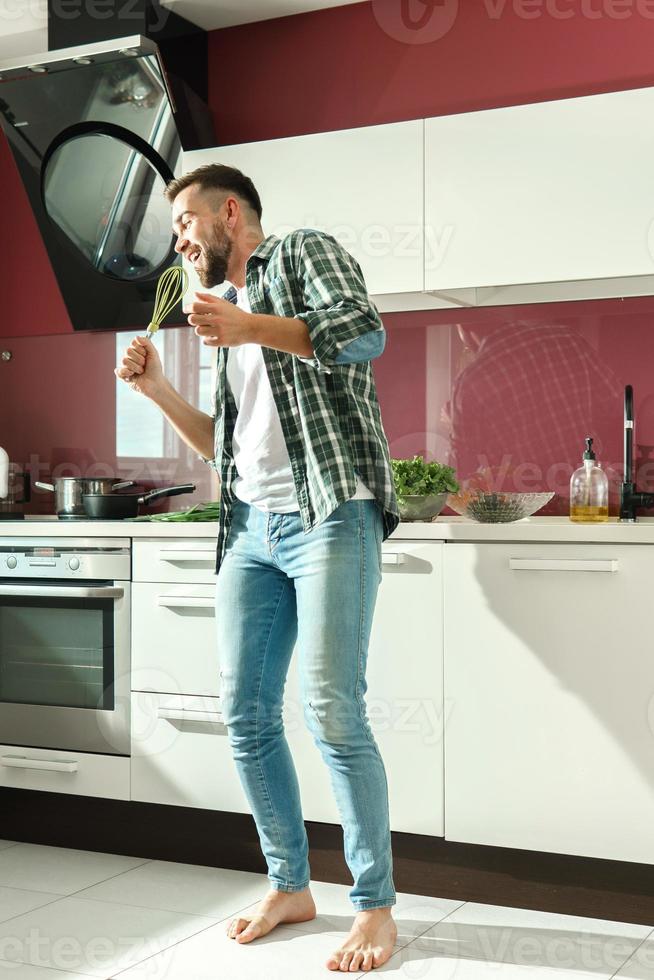 Handsome man dancing and singing on the kitchen while cooking during sunny morning photo