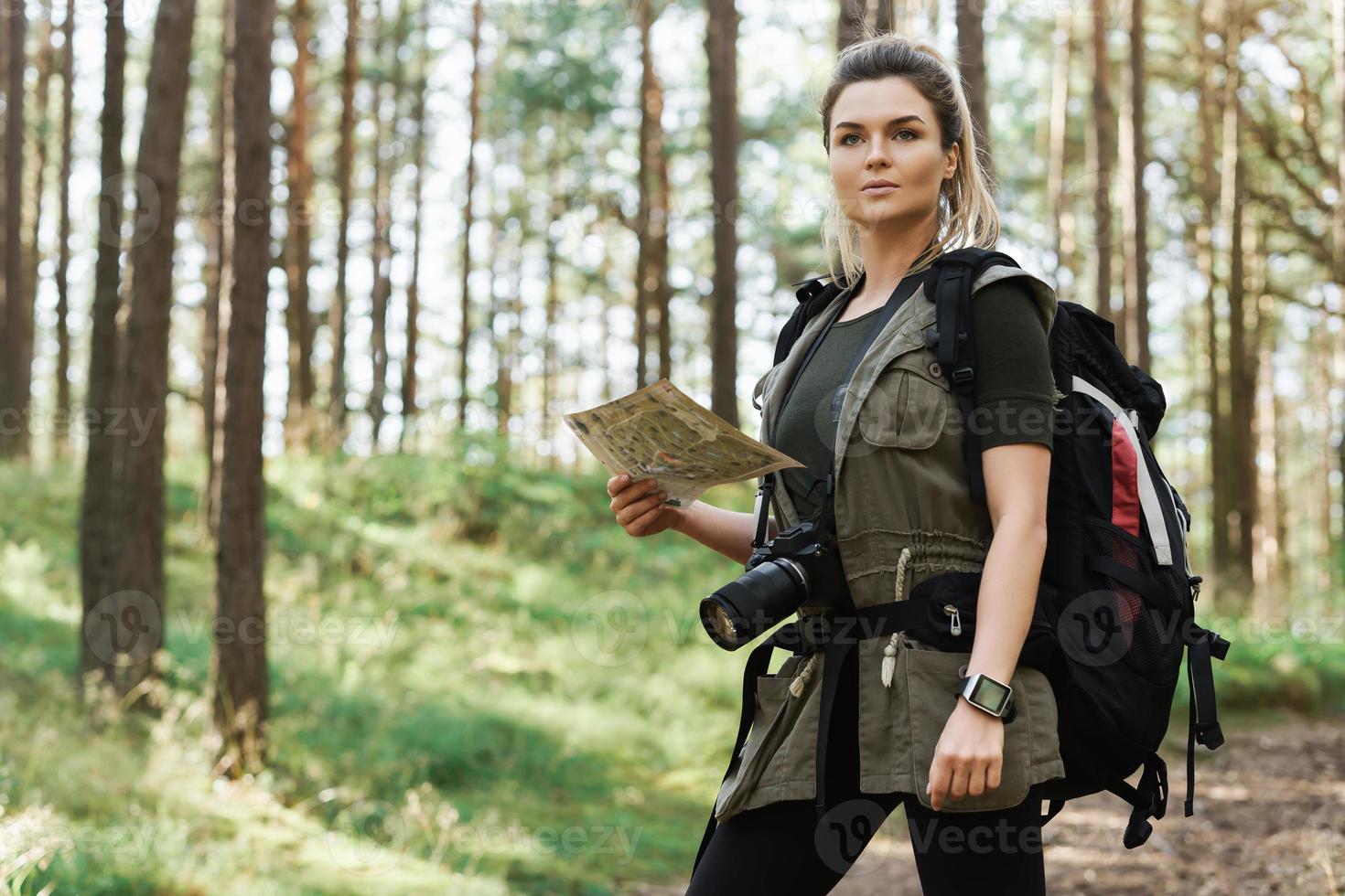 Female hiker with big backpack using map for orienteering in the forest photo