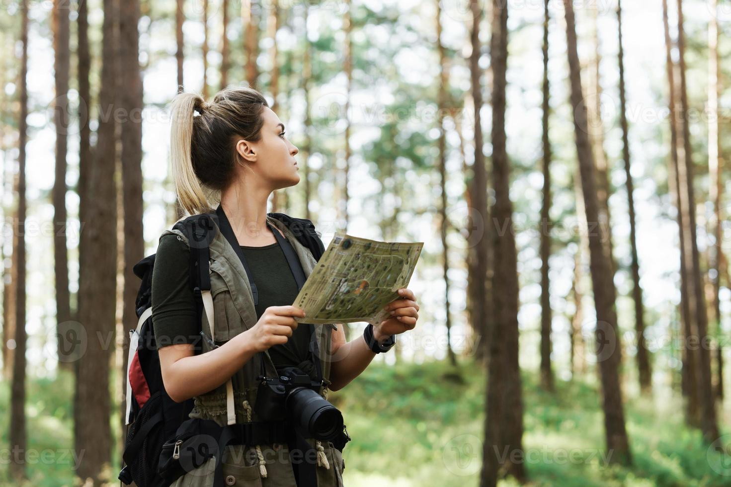 Female hiker with big backpack using map for orienteering in the forest photo