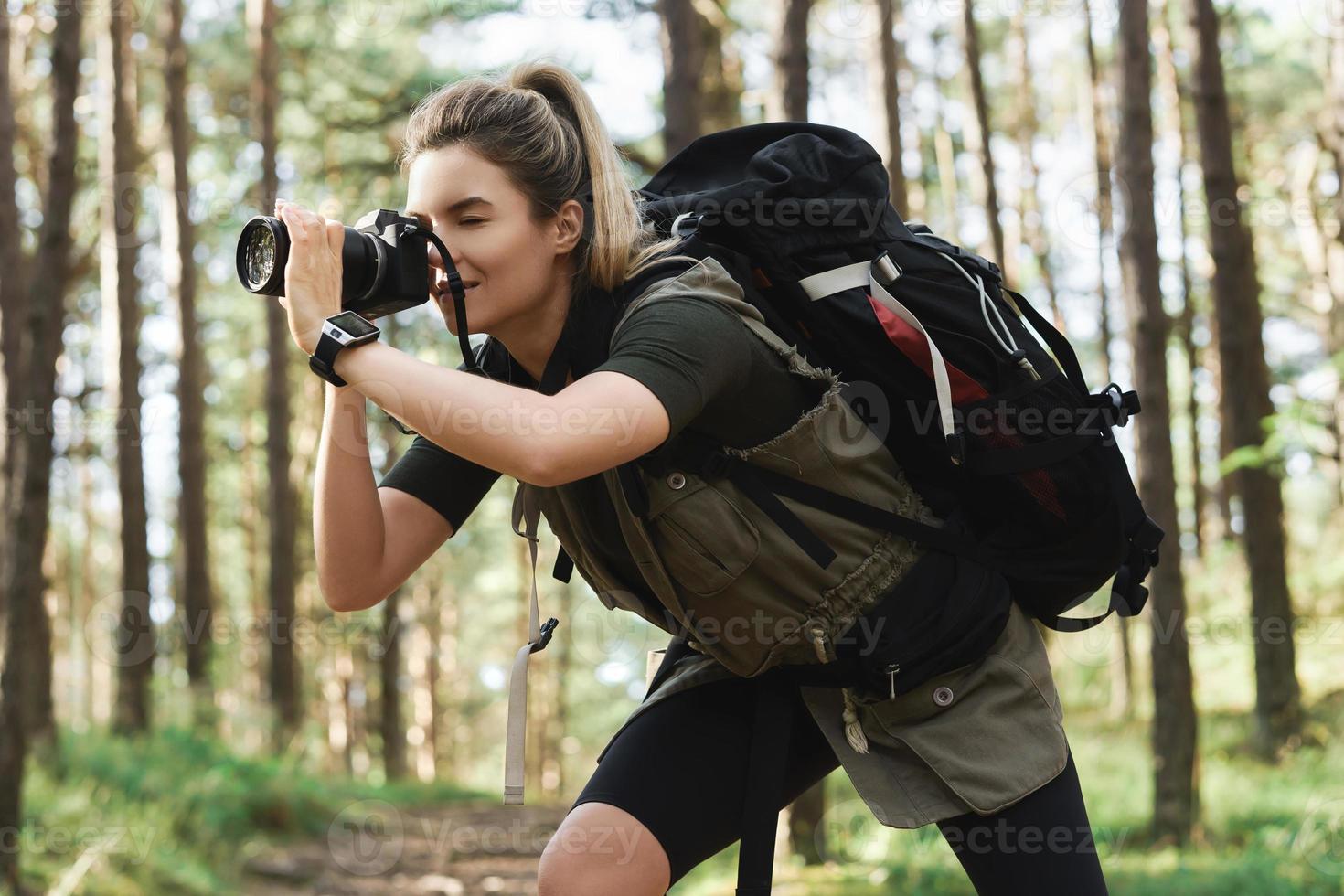Hiker taking photos using  modern mirrorless camera in green forest