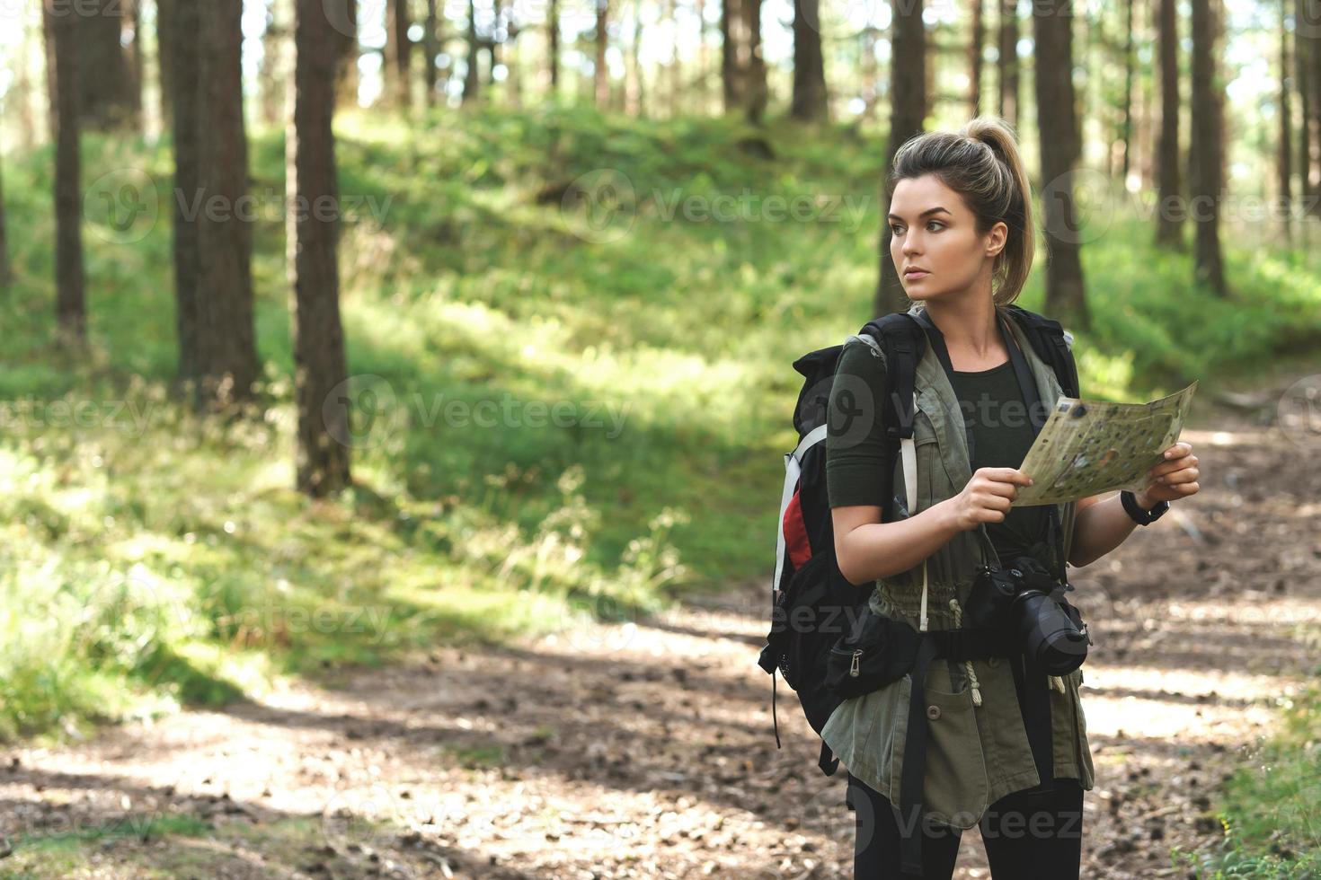 Female hiker with big backpack using map for orienteering in the forest photo