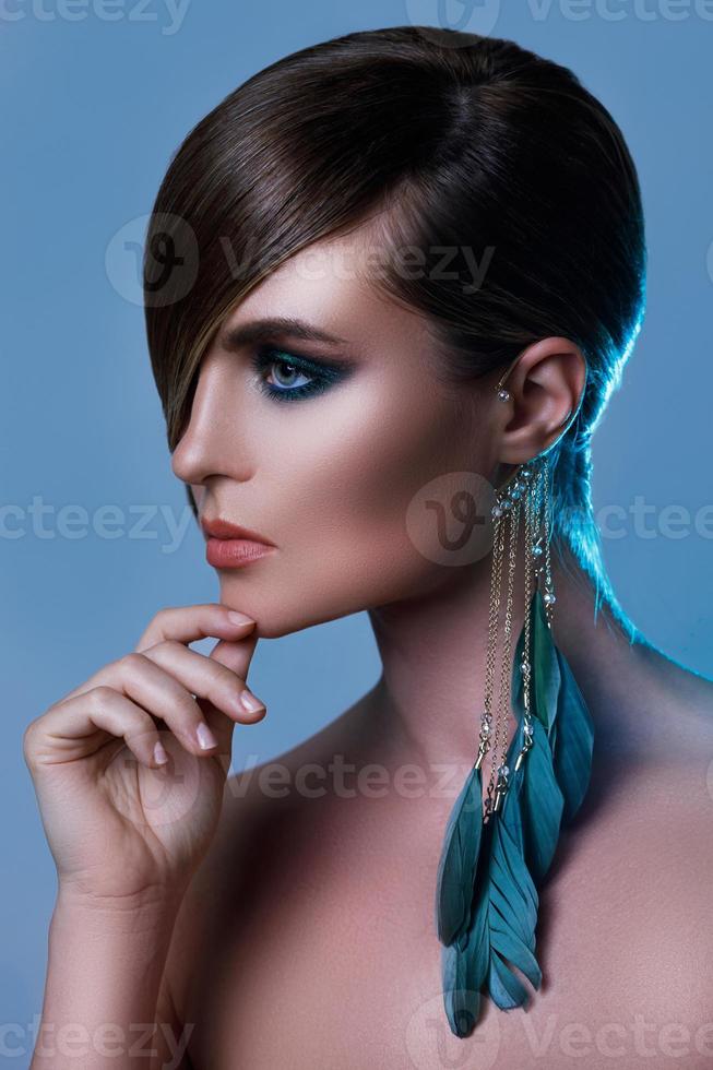 Model in stylish image with sleek hair covering one eye and feather earring photo