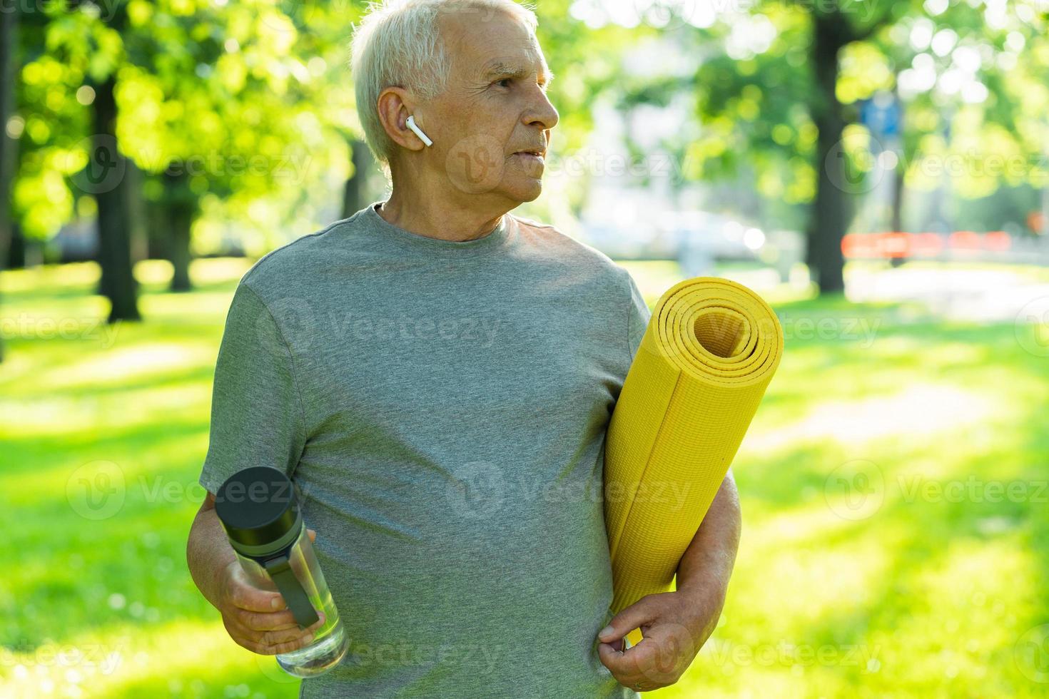 Active elderly man with a exercise mat and bottle of water in green city park photo