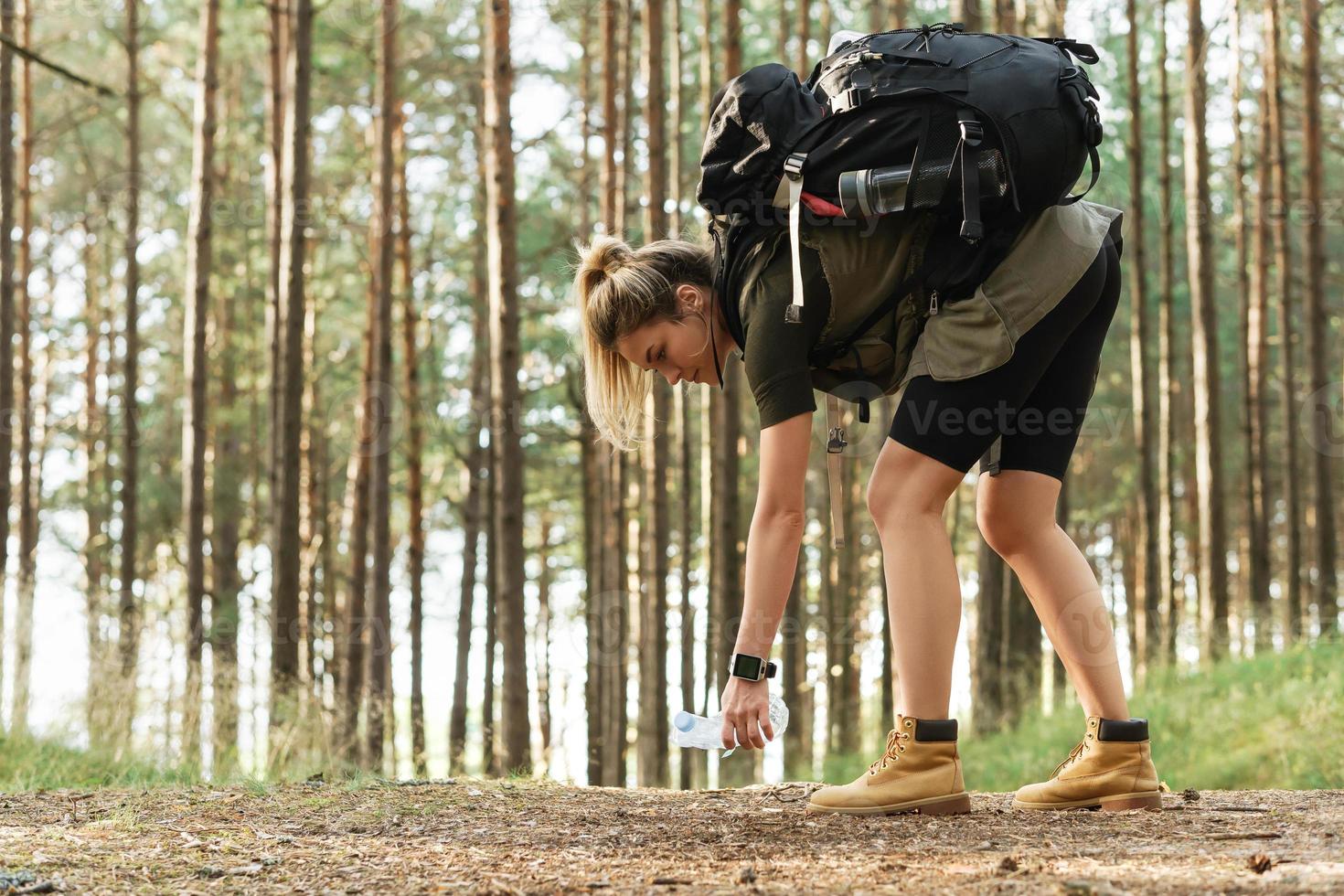 Female hiker collecting plastic waste in green forest photo