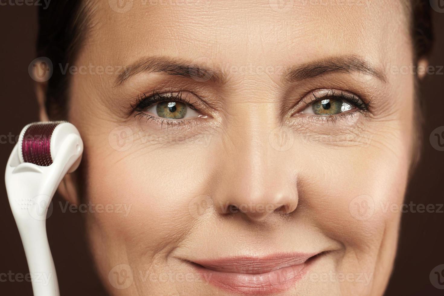 Middle aged woman using mesoroller for her facial skin. photo