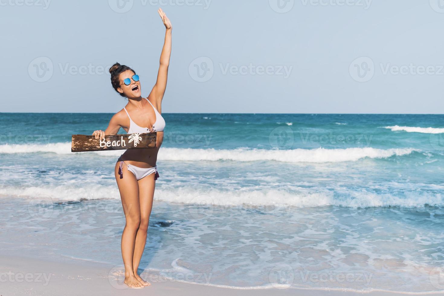 Sexy woman wearing swimsuit with old wooden sign on the beach photo