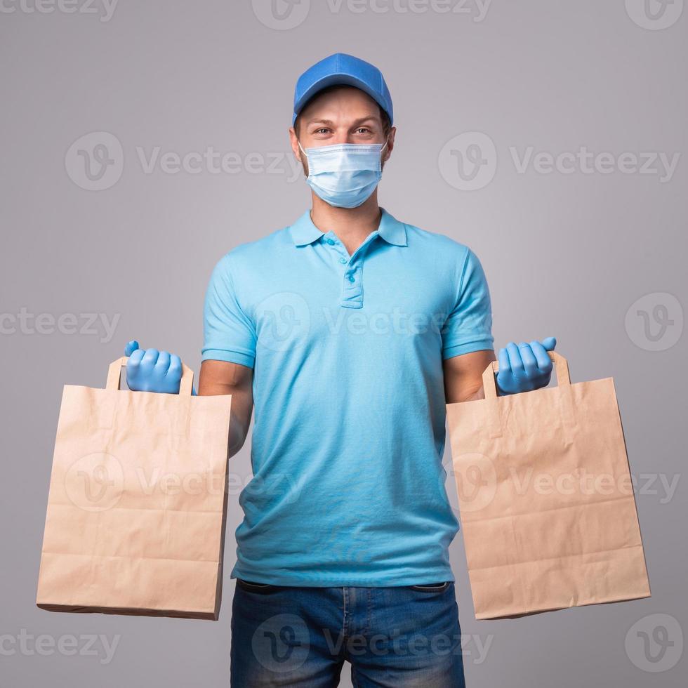 el joven repartidor lleva una máscara de prevención y guantes con bolsas de papel foto