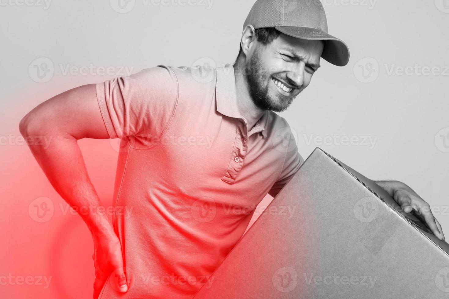 Delivery man suffering from a back pain while carrying heavy box photo