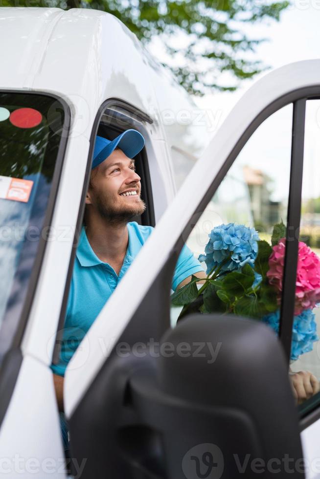 el mensajero dentro de la furgoneta blanca durante la entrega de flores está esperando a un cliente foto