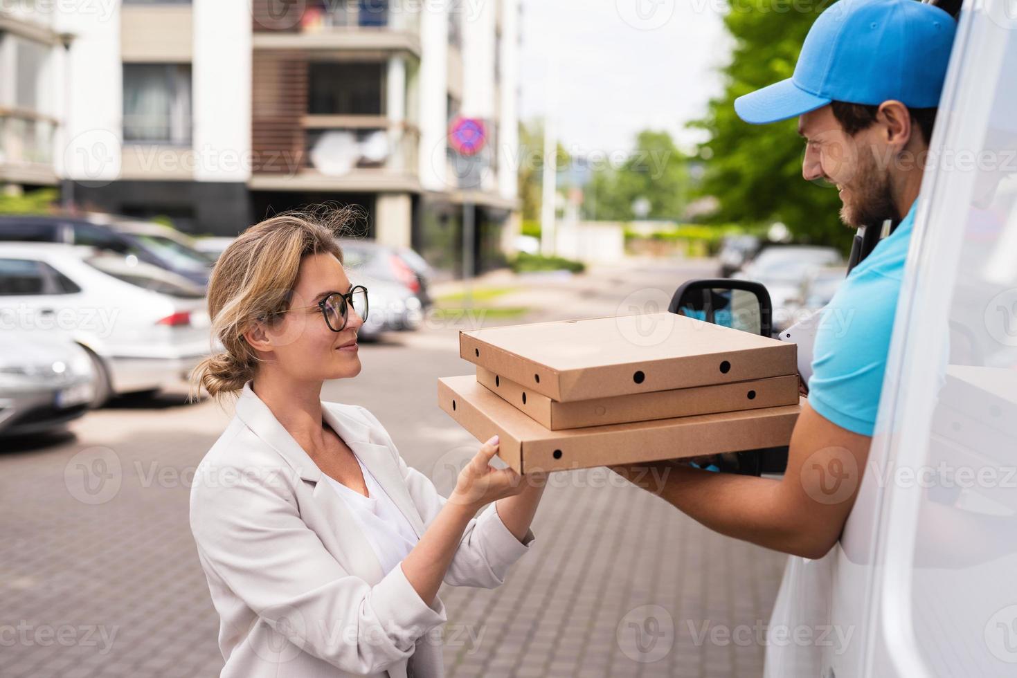 Delivery man in a white van delivers pizza to a woman client photo