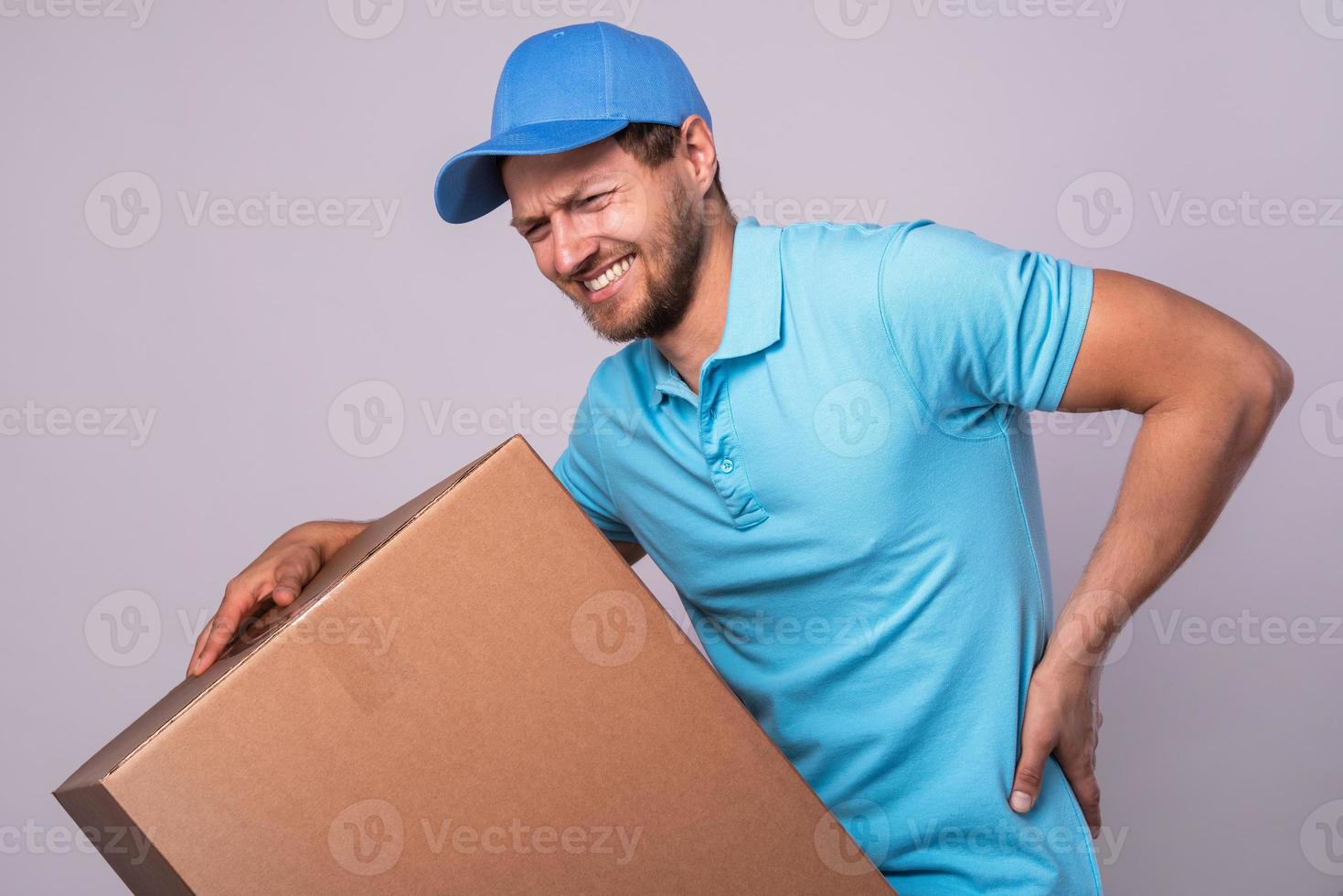 Delivery man suffering from a back pain while carrying heavy box photo