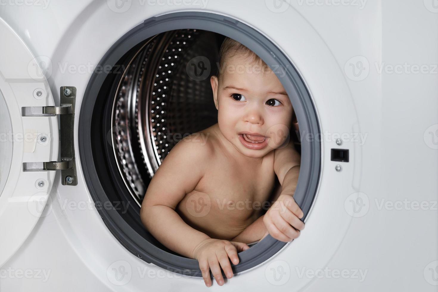 Scared baby boy sitting inside the washing machine photo